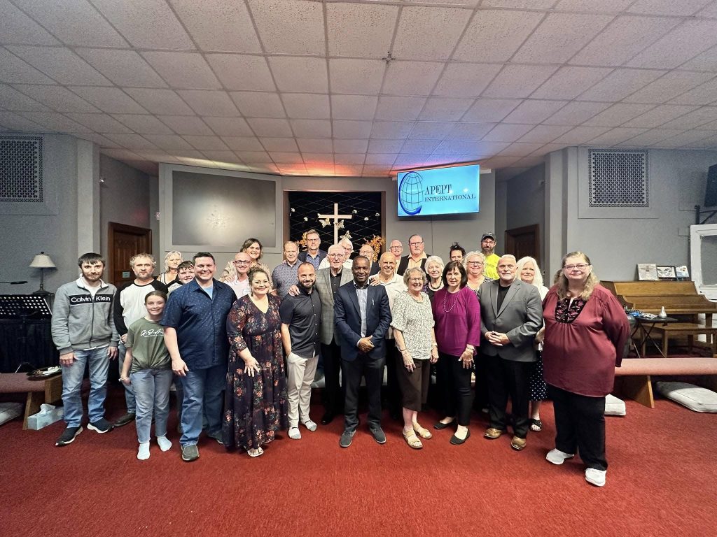 A group gathered inside a church beneath an APEPT International screen