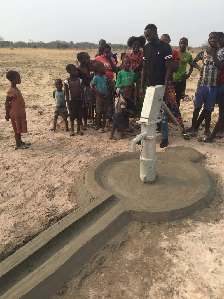 Adults and children gathered around a hand-operated water pump on a concrete well platform